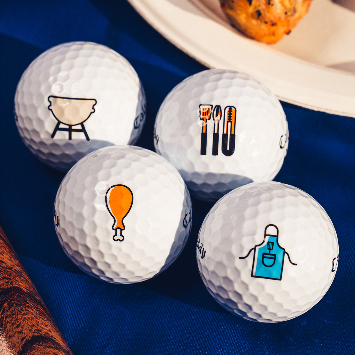 Four Callaway Supersoft Grillmaster golf balls with grill, utensils, drumstick and apron designs